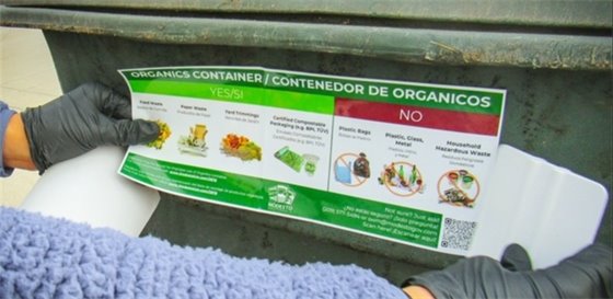 City of Modesto Staff putting a composting instruction label on a green garbage bin. 