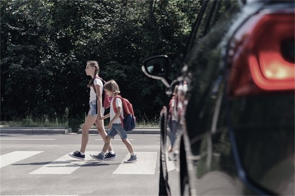 Photo of two kids crossing a crosswalk in front of a black car.